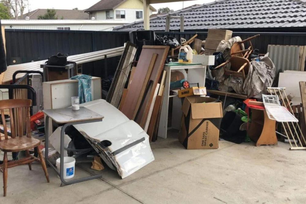 Backyard scene with a disorganized pile of junk, including a chair and table, representing a junk removal service in Los Angeles.
